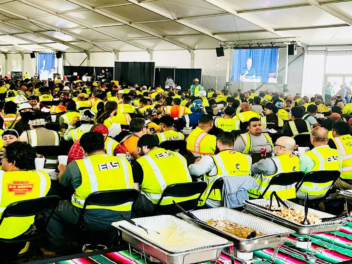 Construction crews in high-visibility vests seated for a catered meal in a temporary dining hall
